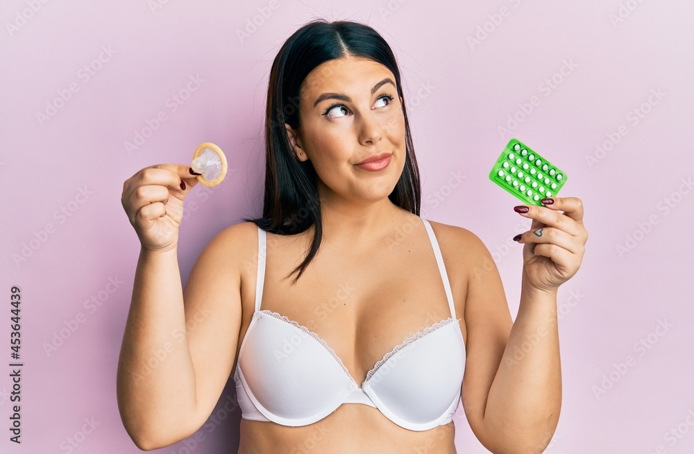Beautiful woman holding condom and birth control pills smiling