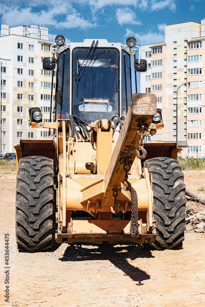 Powerful wheel loader for transporting bulky goods at the construction site of a modern residential area. Construction equipment for lifting and moving loads.