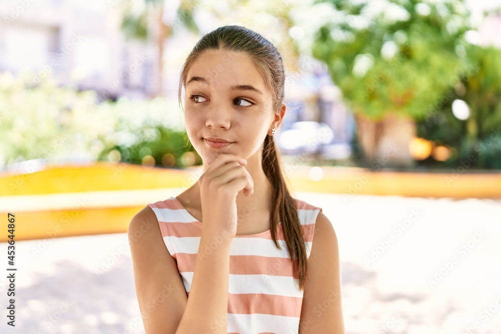 Young teenager girl outdoors on a sunny day serious face thinking about question with hand on chin, thoughtful about confusing idea