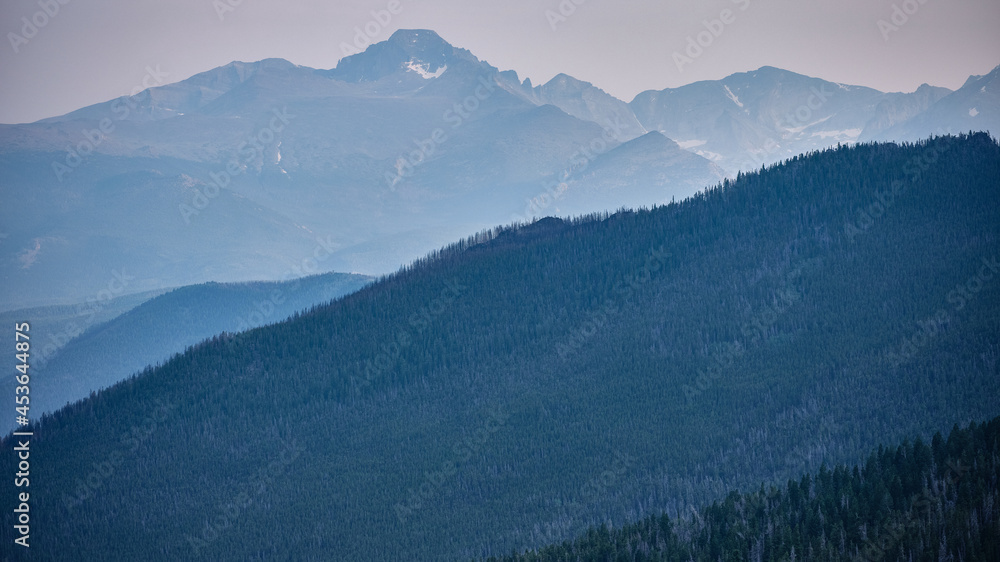 Rocky Mountains and forest trees shrouded in haze and smoke due to burning forest fires