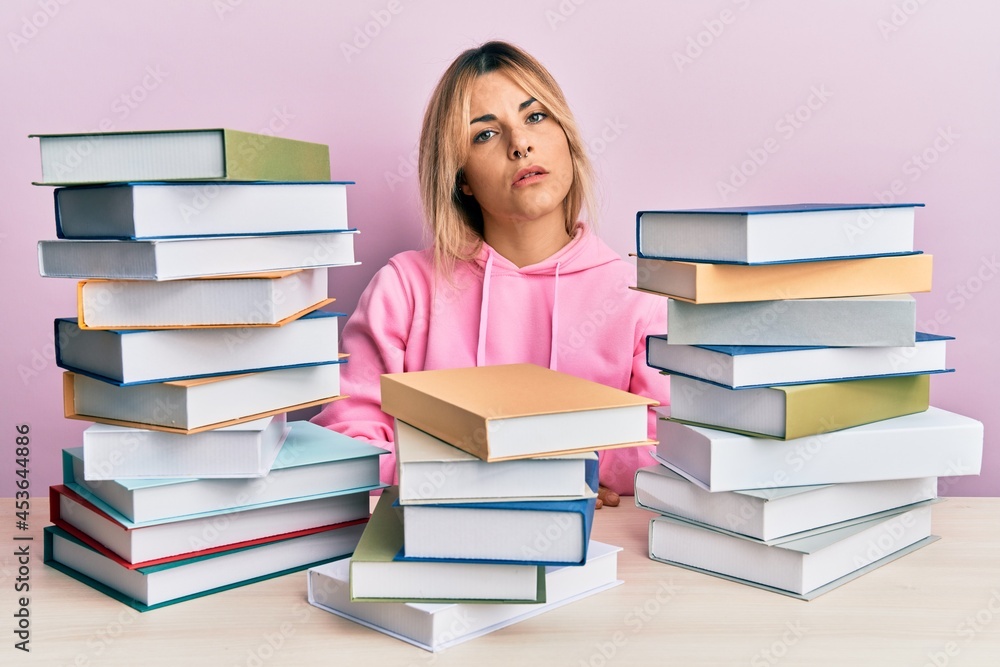 Young caucasian woman sitting on the table with books looking sleepy and tired, exhausted for fatigue and hangover, lazy eyes in the morning. Young caucasian woman sitting on the table with books looking sleepy and tired, exhausted for fatigue and hangover, lazy eyes in the morning.