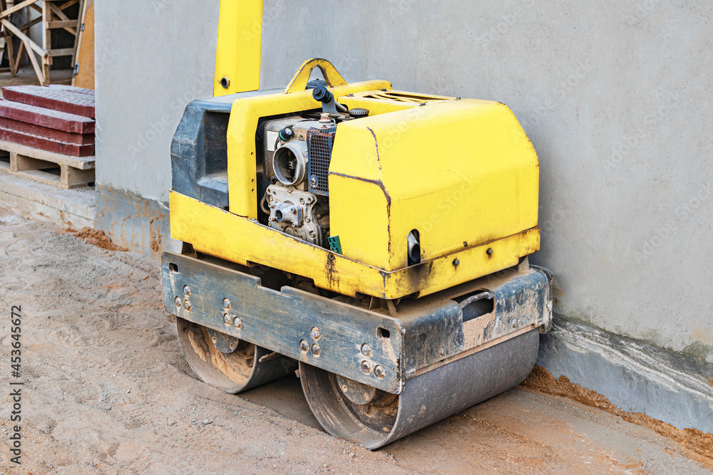 Manual compact asphalt roller for tamping soil at a construction site.