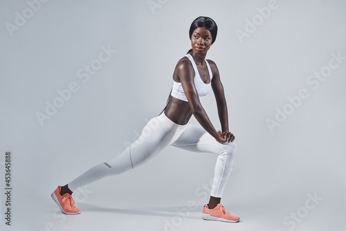Fototapeta Naklejka Na Ścianę i Meble -  Beautiful young African woman in sports clothing stretching against gray background