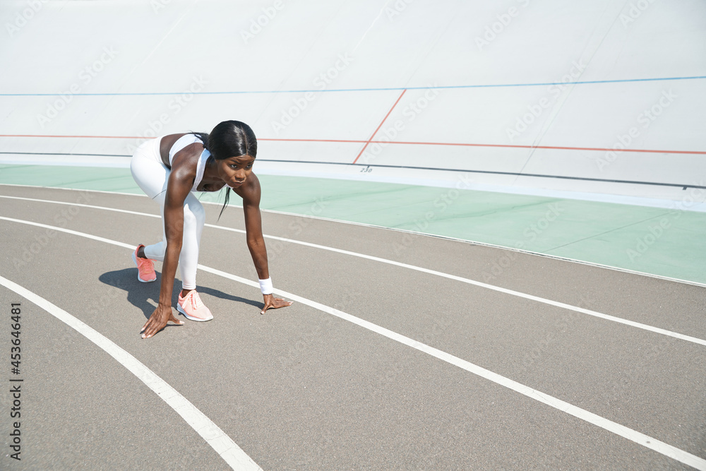 Beautiful young African woman standing at starting position on running track outdoors Beautiful young African woman standing at starting position on running track outdoors