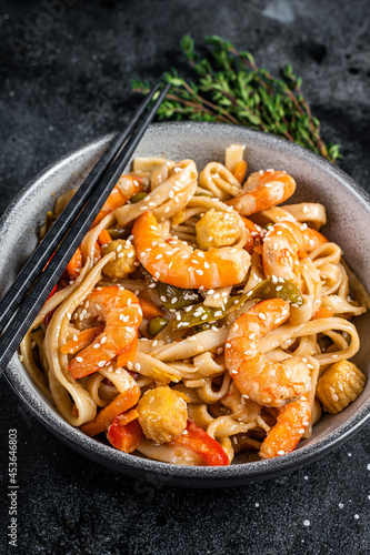 Stir-fry udon seafood noodles with shrimp prawns in a bowl. Black background. Top view