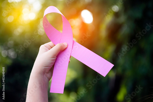 Pink plastic ribbon holding in hand of woman, blurred background, concept for supporting the breast cancer campaign of woman who is sick from breast cancer around the world.