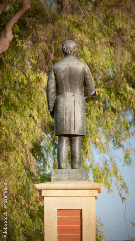 Escultura de espaldas en un pedestal en un parque junto a un árbol