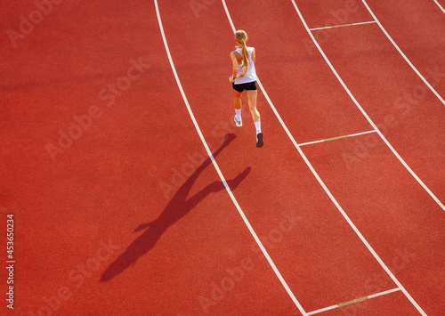 young woman in sportswear runs along the track of the stadium, rear view. sports training and exercise. healthy lifestyle