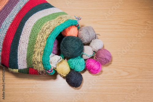 Ovillos de lana de diferentes colores y tamaños saliendo de un saco hecho a mano tejido de lana, sobre un fondo de madera. Crochet, ganchillo. Bolas de hilo. Madejas.