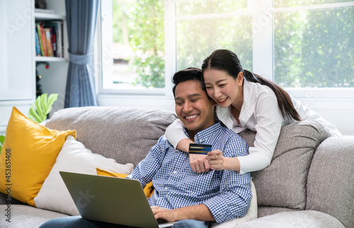 Pleasant family couple sitting looking at laptop screen. Happy young  spouse web surfing, making purchases online or booking flight tickets.