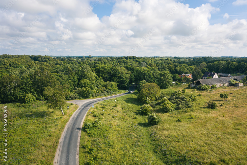 Asphalt road through summer field and forest near farmland. Aerial view