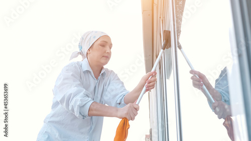 Side view of a woman in a scarf washes the window with a rubber scraper, sunlight