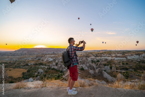 Man takes a picture, photo on smartphone. Tourist attraction balloon flight on background. Entertainment, tourism an vacation. Travel tour. Goreme, Cappadocia, Turkey.