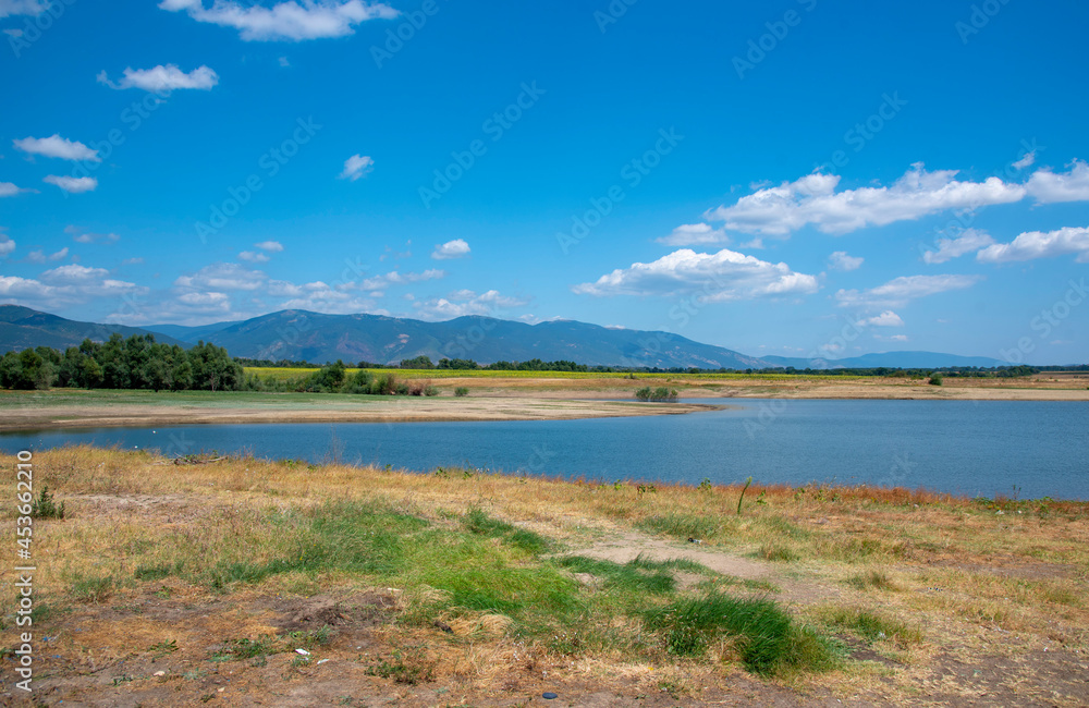 View of the blue lake against the background of the mountains on a clear sunny summer day. View of the blue lake against the background of the mountains on a clear sunny summer day.