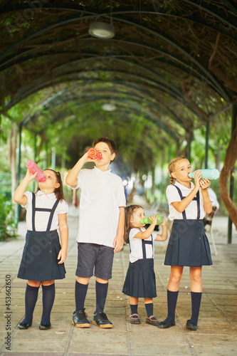 Four elementary school students stand drinking water in park