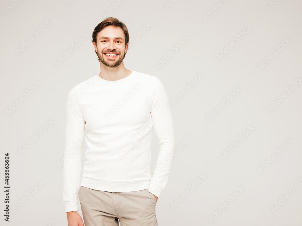 Portrait of handsome smiling hipster lumbersexual businessman model wearing casual white sweater and trousers. Fashion stylish man posing against grey background in studio Portrait of handsome smiling hipster lumbersexual businessman model wearing casual white sweater and trousers. Fashion stylish man posing against grey background in studio
