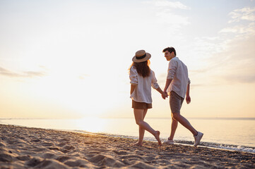 Full body back view young lovely couple two friends family man woman in casual clothes hold hands walking stroll together at sunrise over sea beach ocean outdoor exotic seaside in summer day evening.