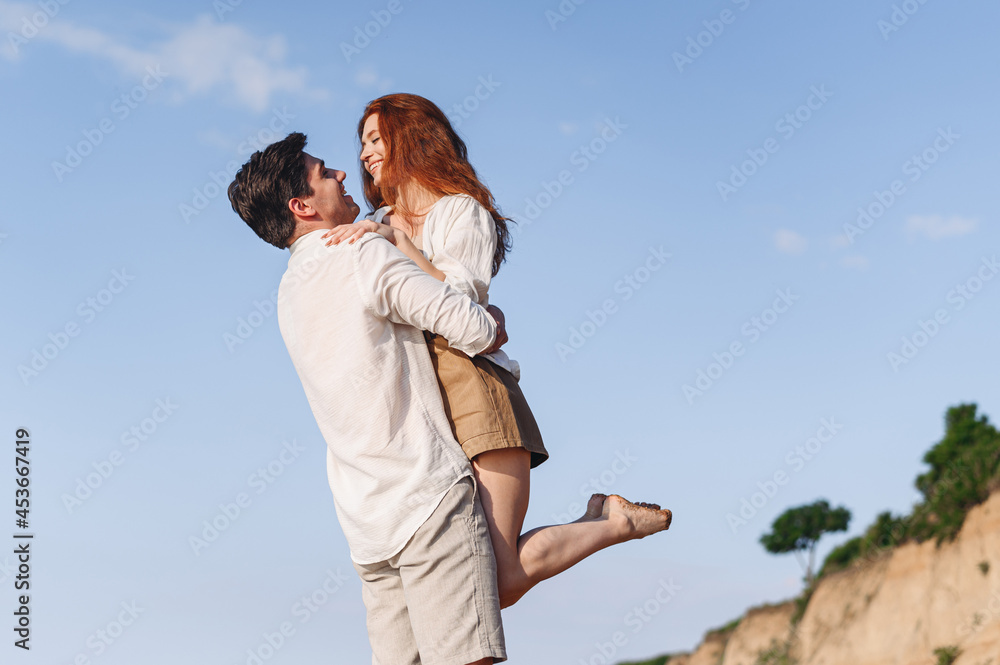 Side view fun happy young couple two friends family man woman in white clothes boyfriend hug hold girlfriend at sunrise over sea sand beach ocean outdoor exotic seaside in summer day sunset evening. Side view fun happy young couple two friends family man woman in white clothes boyfriend hug hold girlfriend at sunrise over sea sand beach ocean outdoor exotic seaside in summer day sunset evening.
