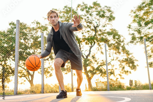 Young cool sunlit european sporty sportsman man 20s wear sports clothes doing handling drills training holding in hand ball play at basketball game playground court Outdoor courtyard sport concept © ViDi Studio