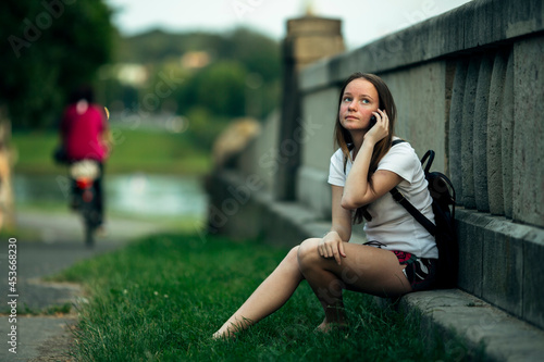 A teenage girl is talking on the phone sitting outdoors.