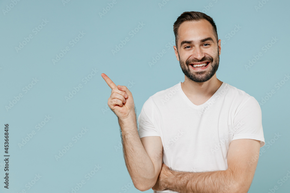 Young smiling happy fun satisfied man 20s wear casual white t-shirt point index finger aside on workspace area mock up copy space isolated on plain pastel light blue color background studio portrait Young smiling happy fun satisfied man 20s wear casual white t-shirt point index finger aside on workspace area mock up copy space isolated on plain pastel light blue color background studio portrait
