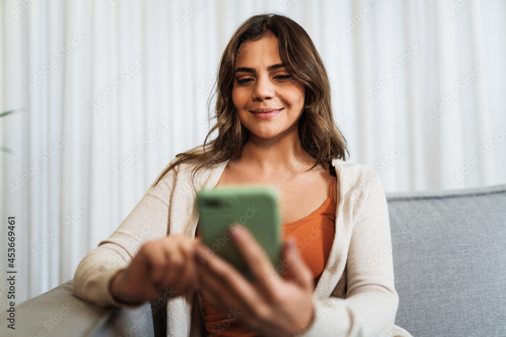 Happy Latin lady relax at home alone sit on room pose share good news at social media via cellphone. Smiling woman enjoy weekend order goods food online in phone app. Happy Latin lady relax at home alone sit on room pose share good news at social media via cellphone. Smiling woman enjoy weekend order goods food online in phone app.
