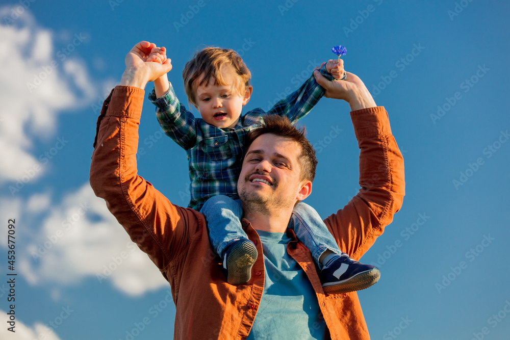 little boy sits on his father's shoulders on blue sky background little boy sits on his father's shoulders on blue sky background