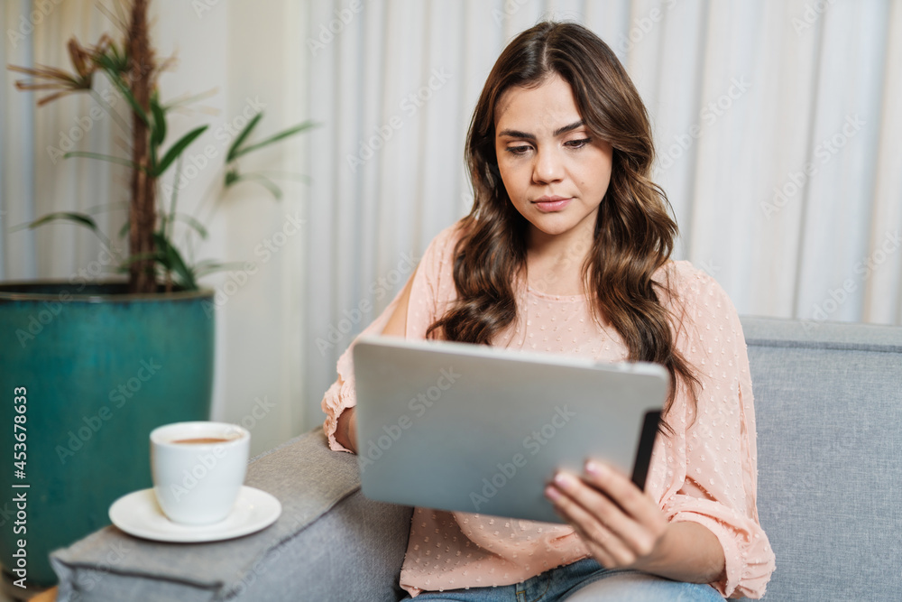 Happy Latin lady relax drinking coffee at home alone sit on room using digital tablet. Happy Latin lady relax drinking coffee at home alone sit on room using digital tablet.