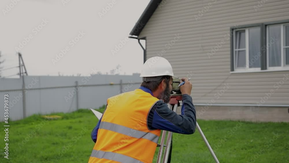 A male engineer works with the optical level on site. A builder in a helmet looks into an optical device. A male engineer works with the optical level on site. A builder in a helmet looks into an optical device.