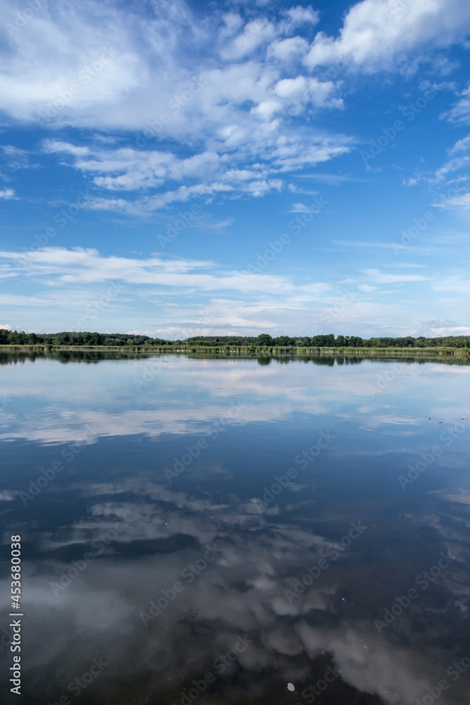 Blue sky covered with white clouds and sky reflection in the calm water of Pilka lake