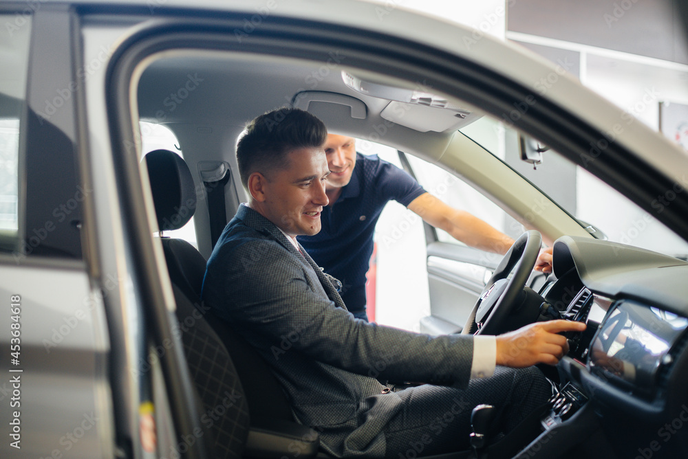 A young businessman with a salesman looks at a new car in a car dealership. Buying a car A young businessman with a salesman looks at a new car in a car dealership. Buying a car