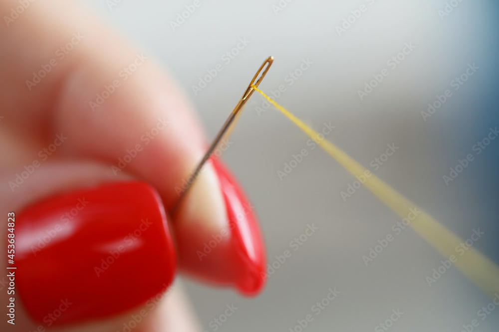 Hands with manicure hold a needle and thread Hands with manicure hold a needle and thread