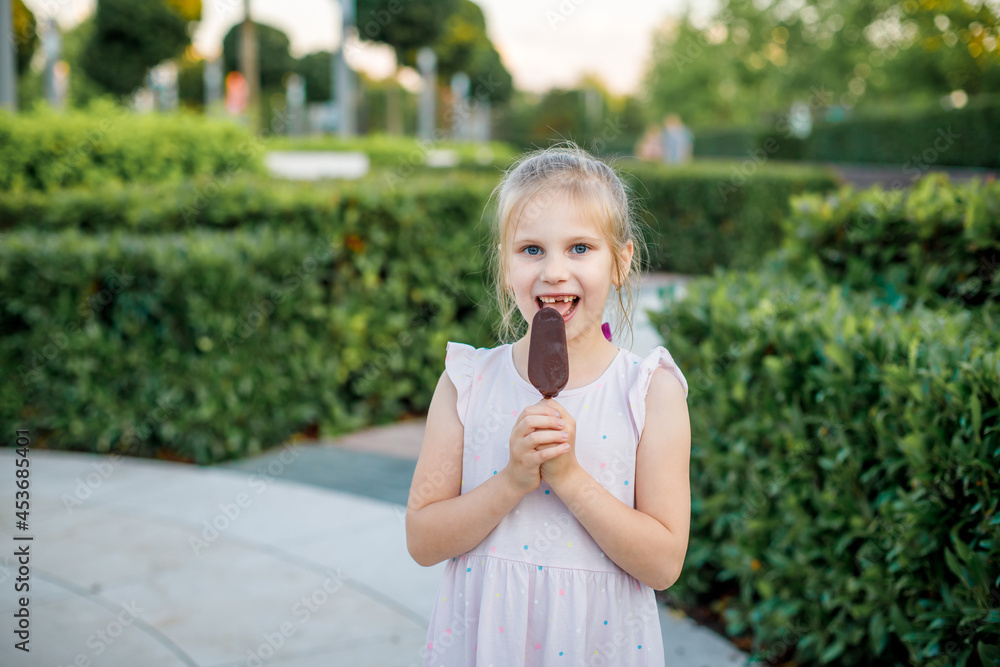 girl in a light dress eats popsicle ice cream in a city park. Children's rest in the summer. girl in a light dress eats popsicle ice cream in a city park. Children's rest in the summer.