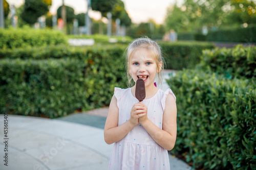 girl in a light dress eats popsicle ice cream in a city park. Children's rest in the summer.
