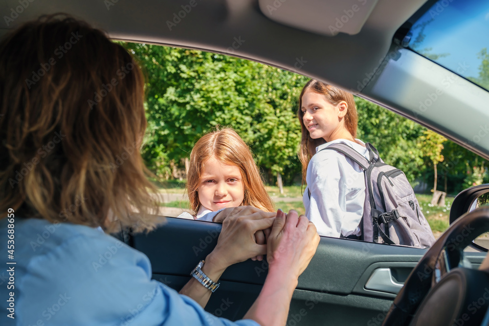 Mother sitting inside the car and leaving her daughters in school uniform at school. Mother sitting inside the car and leaving her daughters in school uniform at school.