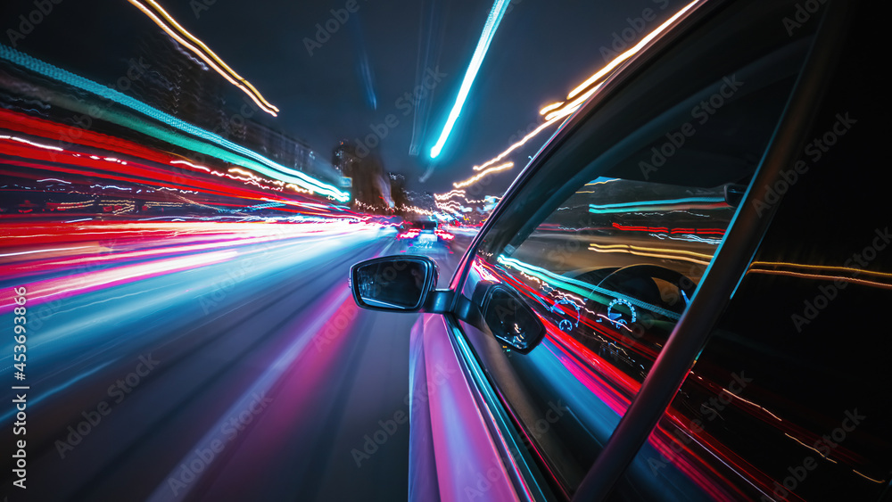 Fototapeta premium Speedy night drive in a big city ending in the underground car parking. Side view from the car window to the road with light trails from vehicles and street lights.