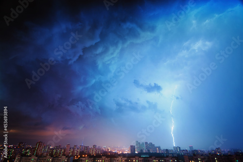 Amazing view of the night storm over the big city  with colorful clouds moving on the sky and bringing first drops of rain  and bright lightnings illuminating the scene.