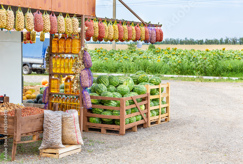 Roadside farmers market selling organic eco foodstuffs against the background of a field with sunflowers. Vegetable oil in bottles, potatoes in nets, watermelons, pumpkin, nuts on the counter.