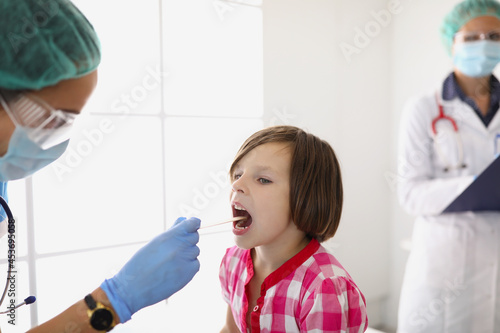 Woman doctor examines the throat of a little girl