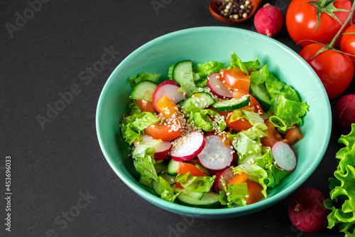 Seasonal vegetable salad from organic farm products on gray background. Mix of tomatoes, cucumbers and radishes.