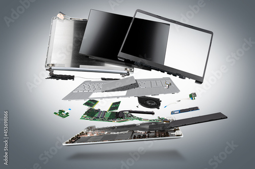 flying parts of a notebook computer. hardware components mainboard cpu processor display RAM cables and cooling fan flying out of silver laptop PC case dark gray exploded view background photo