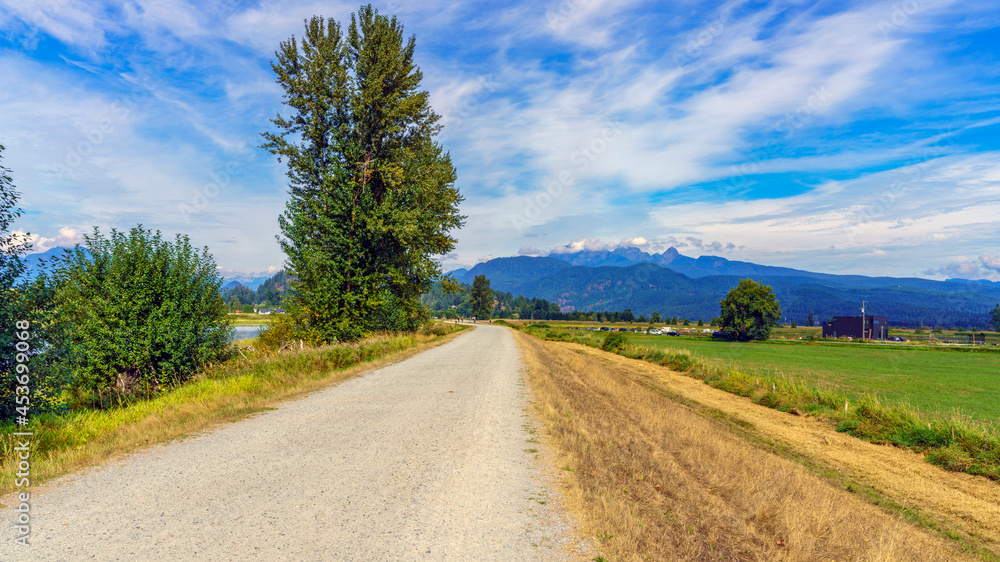 Popular biking/hiking trail alongside Alouette River near Pitt Meadows, BC, with farmland to right and mountains in background
