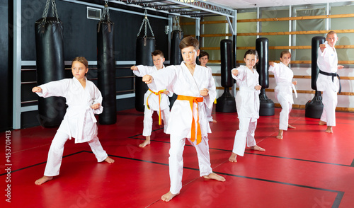 Group of preteen boys and girls doing karate kicks with male coach during karate class