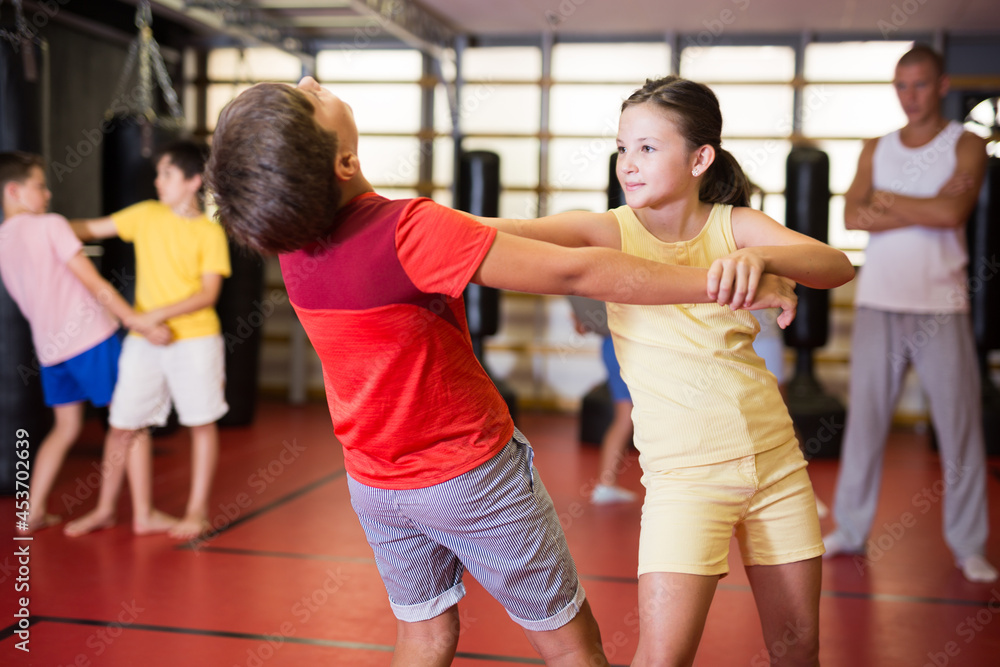 Preteen children practicing in pair self-defence movements with male trainer supervision