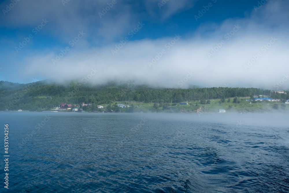 Lake Baikal close to village Port Baikal, Russia. Sunny day view of the high shore and clear lake water with fog