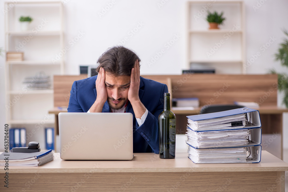 Young alcohol addicted male employee working in the office Young alcohol addicted male employee working in the office