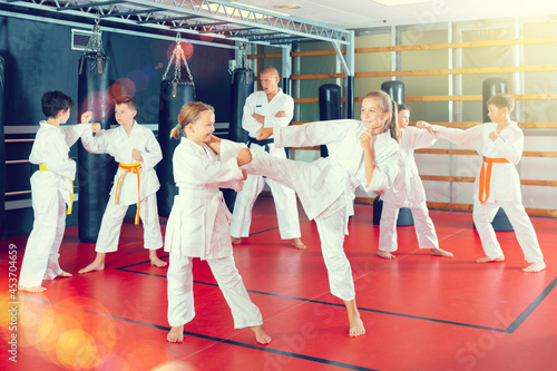 Young girls and boys in kimono and belts sparring during karate training.