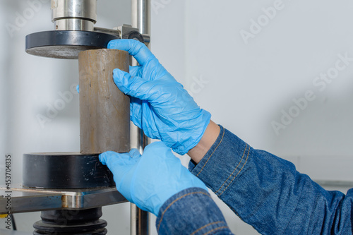 Close up of hands with blue latex gloves placing a clay cylinder in a geological testing machine