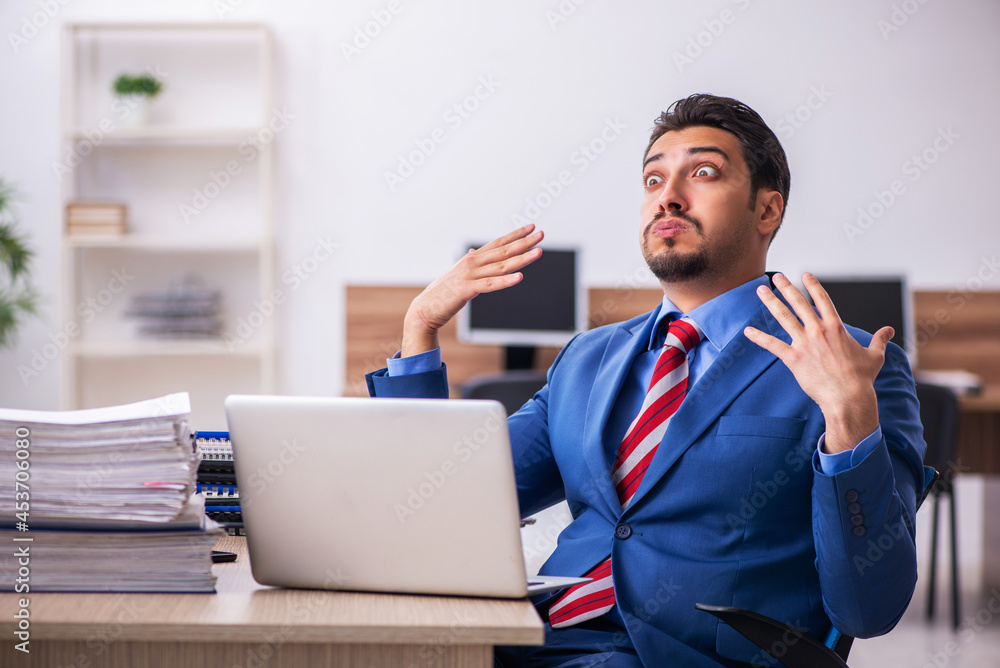 Young male employee unhappy with excessive work at workplace Young male employee unhappy with excessive work at workplace