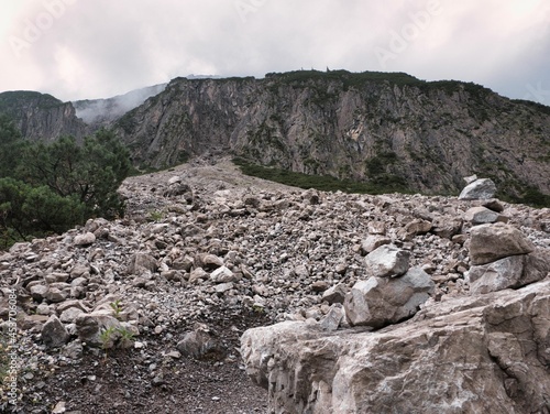 Mondlandschaft in den Alpen in Österreich bei Gramais Richtung Branntweinboden mit von Wanderern hinterlassenen Steinen, Geröll und einer bedrohlichen Felswand bei wolkigem Regenwetter